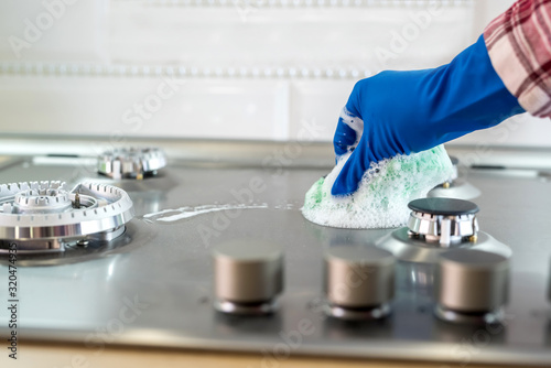 Woman with sponge and rubber protective glove used to wipe down an oven range top. © RomanR