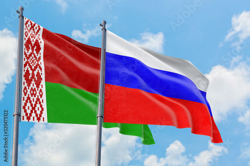 Russia and Belarus flags waving in the wind against white cloudy blue sky together. Diplomacy concept, international relations.