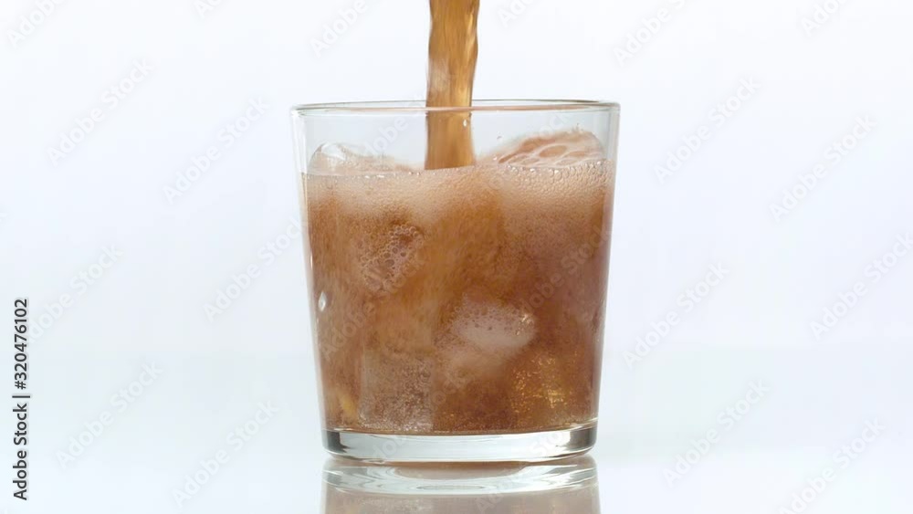 Close up cola pouring into the glass. Fizzy drink with ice cubes and lemon slice in transparent drinking glass against white background. Coke Soda closeup, slow motion