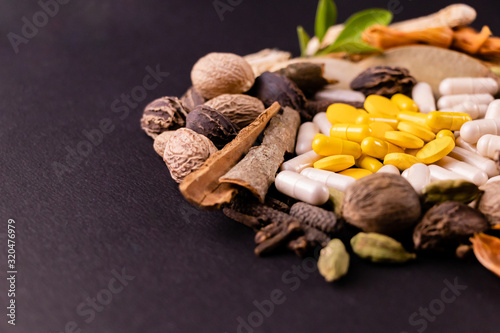 Close-up of yellow herbal capsules, tablets and natural herbs on black background with copy space. Herbal medicines and healthy herbs concept photo