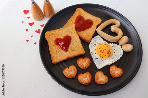 Healthy Love Breakfast on Valentine's Day - fried eggs and brown bread in the shape of a heart, chicken sausages and sweet biscuits. Top view with copy pace. Valentines day greeting.