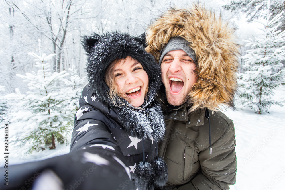 Technologies and relationship concept - Happy smiling couple taking a selfie in a winter forest outside