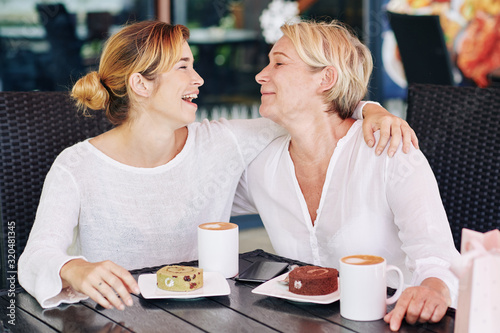 Happy mother and daughter enjoying spending time together in coffeeshop, drinking coffee and having fun