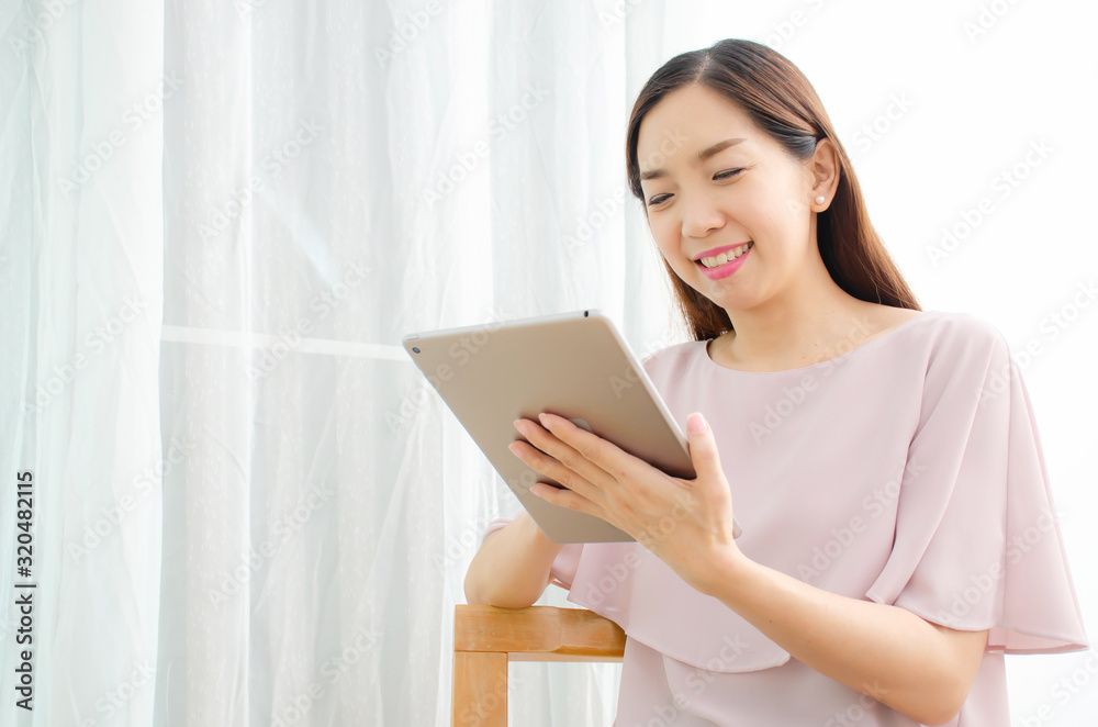 Smiling young female sitting in the armchair in the living room and looking at mobile digital tablet device screen. . Smiling young female sitting in the armchair in the living room and looking at mobile digital tablet device screen. .