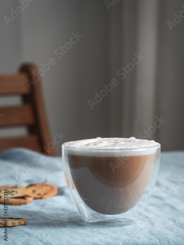 Hot coffee cappuccino in glass with milk foam and crackers on wooden table. Close up. Copy space. Shallow depth of field, focus on the cup.