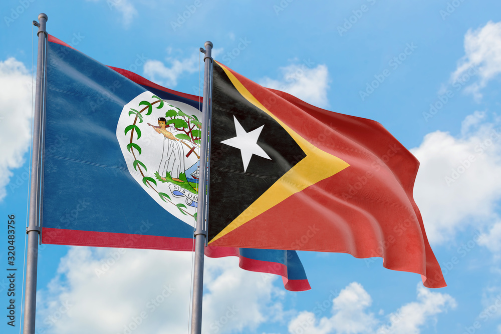 East Timor and Belize flags waving in the wind against white cloudy blue sky together. Diplomacy concept, international relations. East Timor and Belize flags waving in the wind against white cloudy blue sky together. Diplomacy concept, international relations.