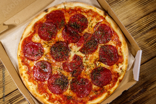 Delicious fresh pizza in cardboard box on a wooden table. Top view. Concept for home delivery of food, fast food, delivery of pizza