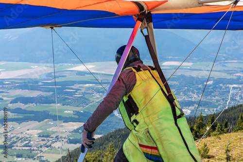 Man with hang-glider preparing to get launched into the air at the peak of a mountain, with Kootenay valley mountains in the background, Canada