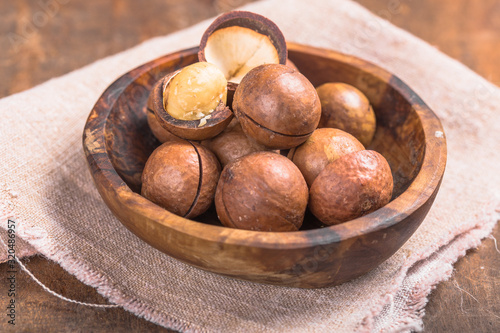 Pile macadamia nuts open kernels and shells in burlap bag on wooden background