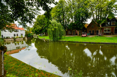 Edam, Netherlands, August 2019. One of the pretty canals of this city: the foliage of the trees is reflected on the water along the banks, pretty houses overlook the shore.
