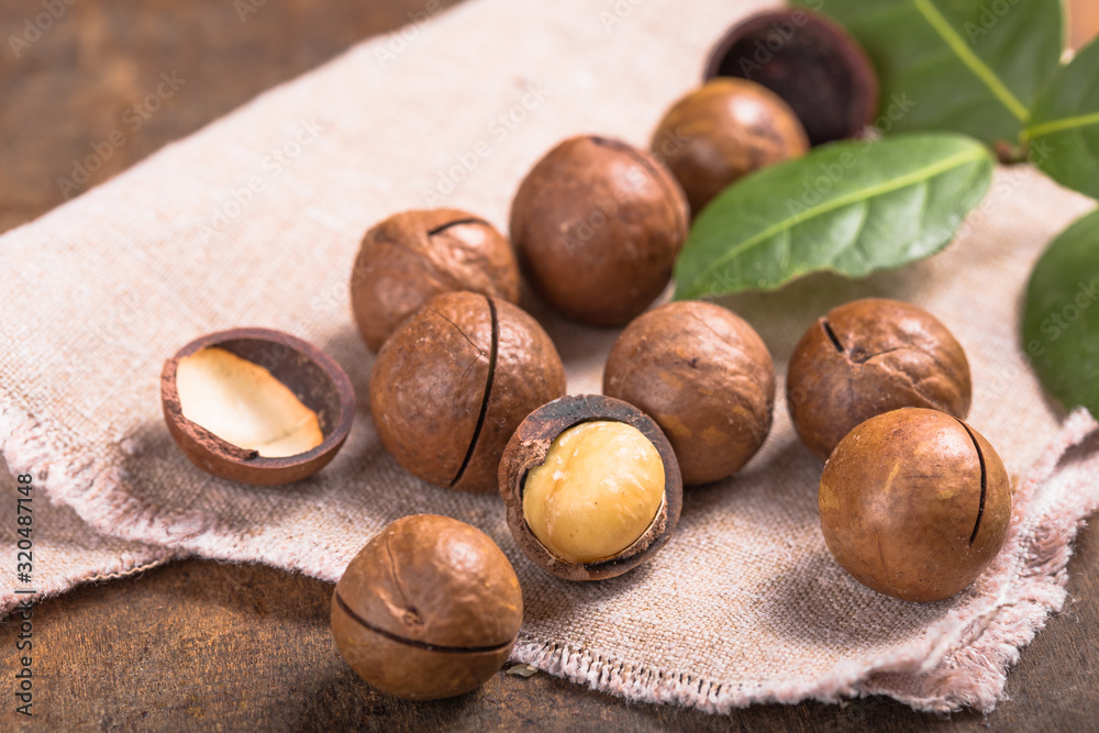 Pile macadamia nuts open kernels and shells in burlap bag on wooden background Pile macadamia nuts open kernels and shells in burlap bag on wooden background