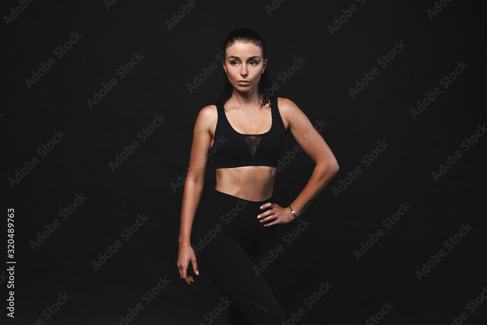 Image of young female model in sportswear standing on black background with copyspace Image of young female model in sportswear standing on black background with copyspace