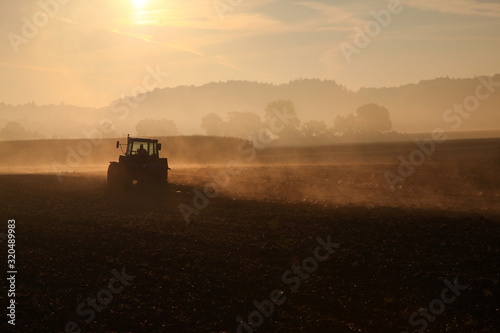 Nebliges Feld in der MOrgensonne auf dem ein Traktor gerade im Gegenlicht den Boden umpflügt © macrossphoto