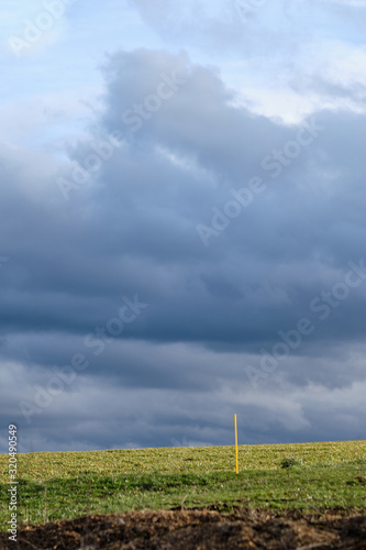 Landscape in the countryside with overcast sky and sunlight illuminating the grass on the fields and some yellow poles sticking in the ground. Seen in Germany