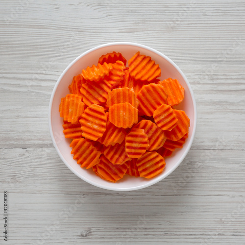 Fresh Raw Organic Carrot Chips in a white bowl over white wooden background, top view. From above, overhead, flat lay. Close-up.