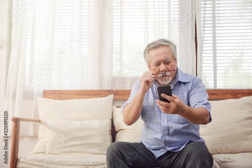 Older men move glasses down to look at the phone in the hand due to Hyperopia problems, which makes vision difficult.Health problems of the elderly.