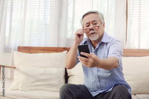 Older men move glasses down to look at the phone in the hand due to Hyperopia problems, which makes vision difficult.Health problems of the elderly.
