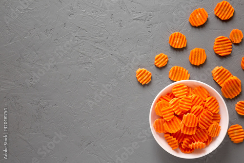 Overhead view, Fresh Raw Organic Carrot Chips in a white bowl over gray surface. From above, overhead, flat lay. Copy space.