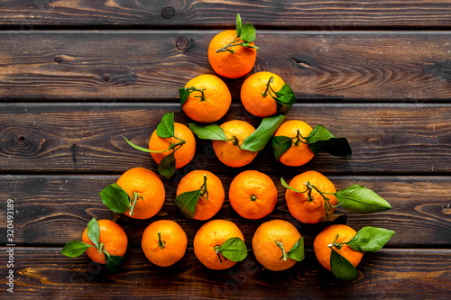 Tangerines with leaves - triangle shape - on dark wooden background top-down copy space