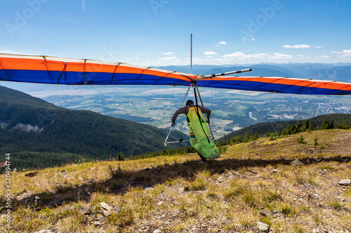 Hang glider pilot running and taking off. Scenic view over Kootenay valley mountains. View from behind to flying Hang glider