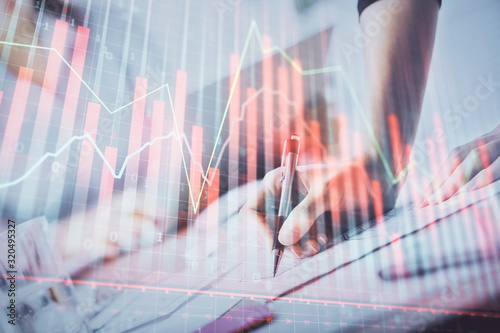 A woman hands writing information about stock market in notepad. Forex chart holograms in front. Concept of research. Double exposure