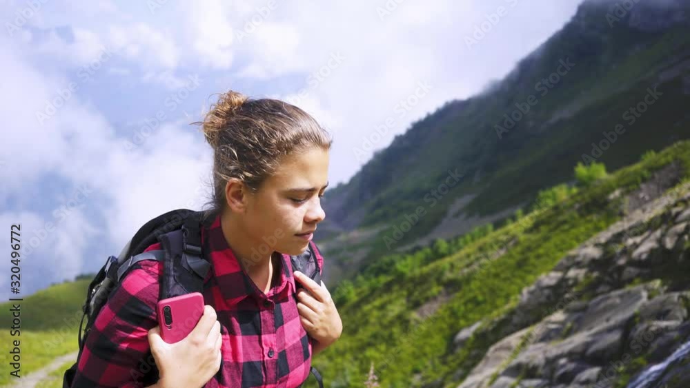 Young woman walking up on rocky path in mountain. Close-up portrait pretty girl with backpack enjoying view waterfall in sun lights while rising on top, camera following with female. Young woman walking up on rocky path in mountain. Close-up portrait pretty girl with backpack enjoying view waterfall in sun lights while rising on top, camera following with female.