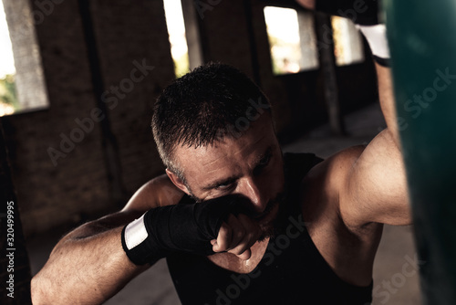 Male boxer punching a boxing bag in warehouse.