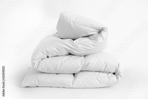 Folded soft white duvet, blanket or bedspread, against white background. Close up photo