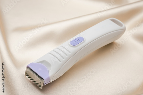 Electric hair trimmer. Personal hygiene item for women. Hair cutting accessory with metal blade on light fabric background.