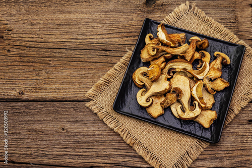 Dried porcini mushrooms. Traditional ingredient for cooking healthy food. Black ceramic plate, sackcloth napkin, old wooden boards background
