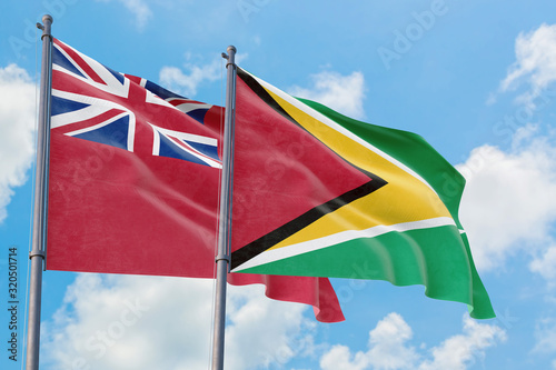 Guyana and Bermuda flags waving in the wind against white cloudy blue sky together. Diplomacy concept, international relations.