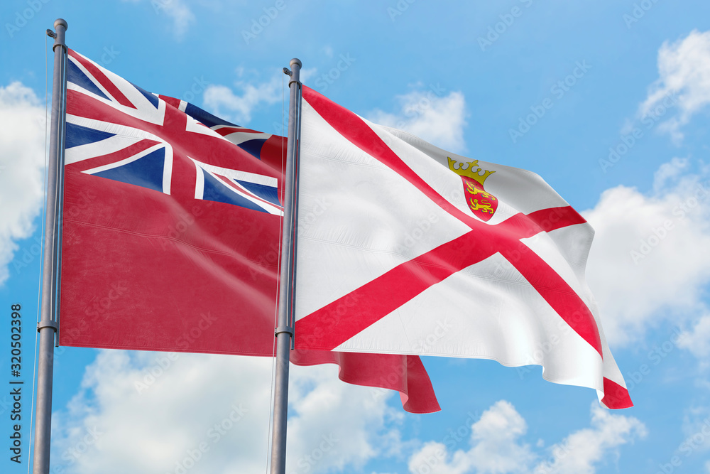 Jersey and Bermuda flags waving in the wind against white cloudy blue sky together. Diplomacy concept, international relations. Jersey and Bermuda flags waving in the wind against white cloudy blue sky together. Diplomacy concept, international relations.