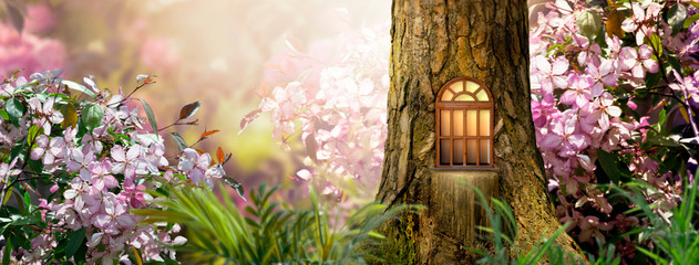 Enchanted fairy tale forest with magical shining window in hollow of fantasy pine tree elf house, blooming fabulous giant pink sakura cherry flower garden, building in wood in fairytale morning light