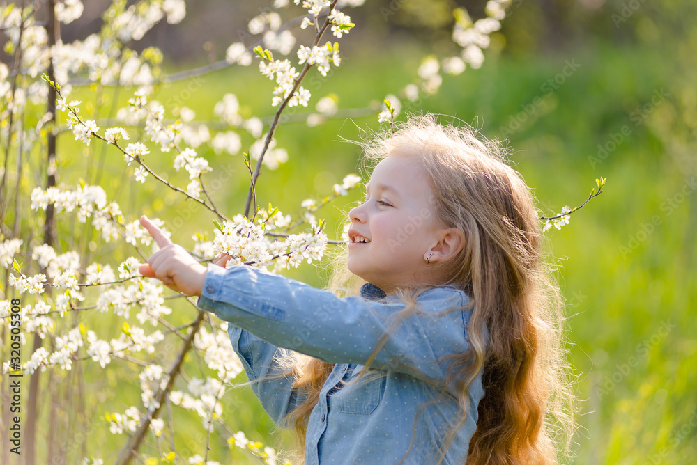 Little cute girl blonde with long hair sniffs a flowering tree branch in the park in spring. Little cute girl blonde with long hair sniffs a flowering tree branch in the park in spring.