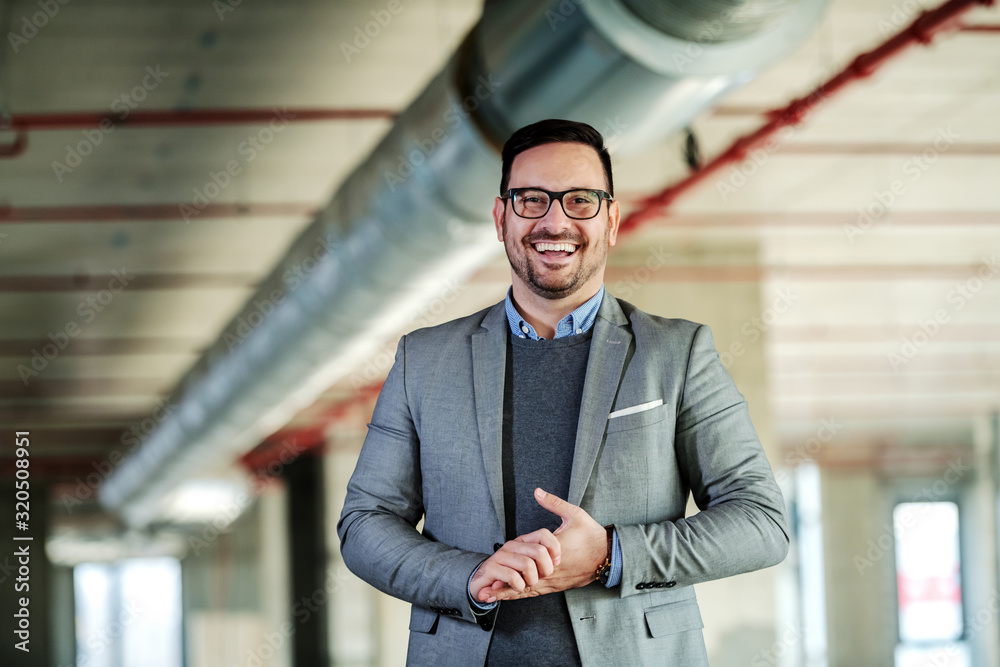 Obraz premium Smiling handsome caucasian businessman in suit is happy to present his own project while standing in building in construction process.