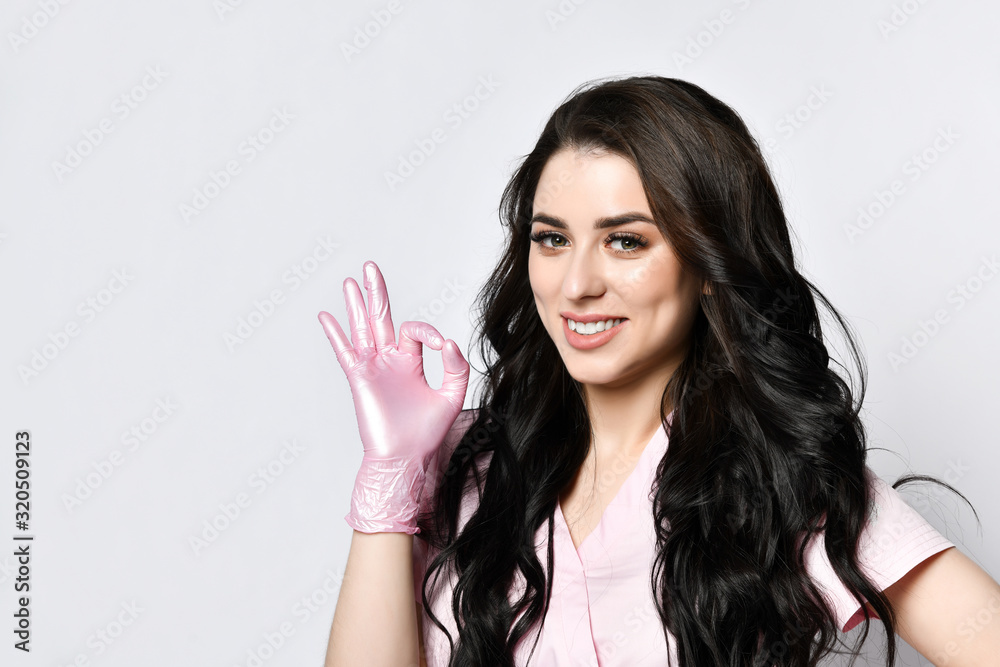 Woman in pink medical clothing and latex gloves posing isolated on white. She smiling and showing okay, hand gesture. Close up Woman in pink medical clothing and latex gloves posing isolated on white. She smiling and showing okay, hand gesture. Close up