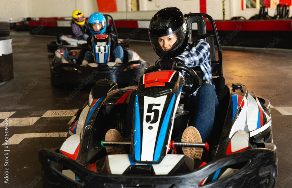 active woman in helmet driving car for karting with other people
