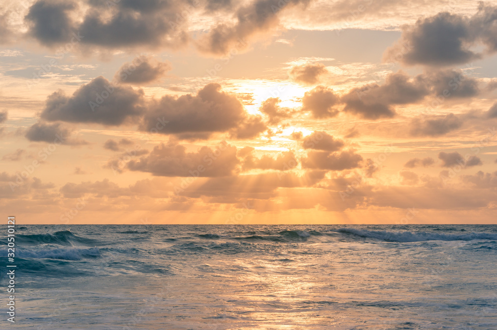 Sunrise seascape with colorful golden orange clouds and soft blue waves