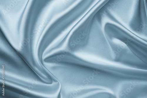 Smooth elegant silver silk fabric background. Metallic gray color of shiny textile, texture. Satin folds, waves pattern. Silky backdrop with curves, luxury fashion.