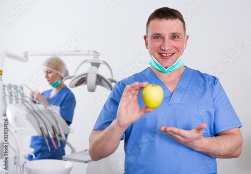 Smiling male dentist with apple at dental clinic