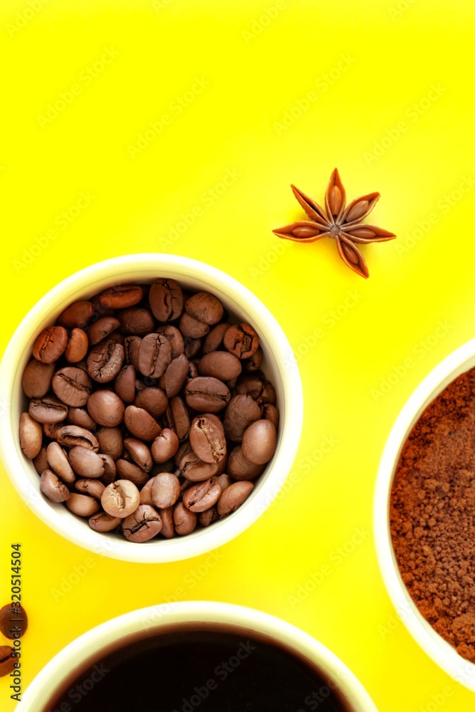 Fototapeta premium Three white cups with ground coffee, coffee beans and black brewed coffee in the rays of bright sunlight, sunset, dawn on a yellow background. Close-up, top view, flat lay, copy space for text.