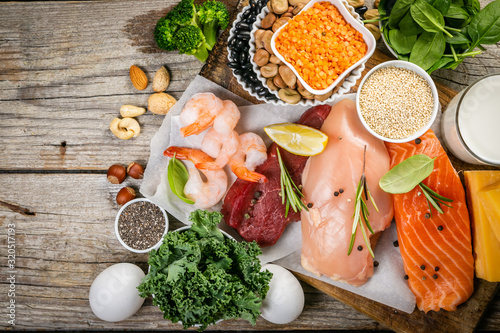 Selection of animal and plant protein sources - fish, meat, beans, cheese, eggs, nuts and seeds, kale, on wood background