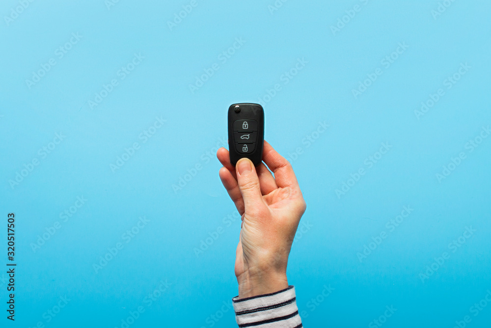 Fototapeta premium Female hand holds car keys on a blue background. Concept car, car rental, gift, driving lessons, driving license. Banner. Flat lay, top view
