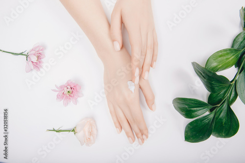 Close-up beautiful sophisticated female hands with pink flowers on white background. Concept hand care, anti-wrinkles, anti-aging cream, spa