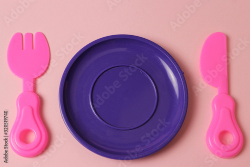 plastic toys tableware plate, fork, knife on pink background