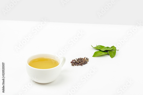 One cup of oolong tea with fresh leaves and a heap of dry green tea on a white background, with copy space for text. Organic herbal, green asian tea for the tea ceremony. Flat lay