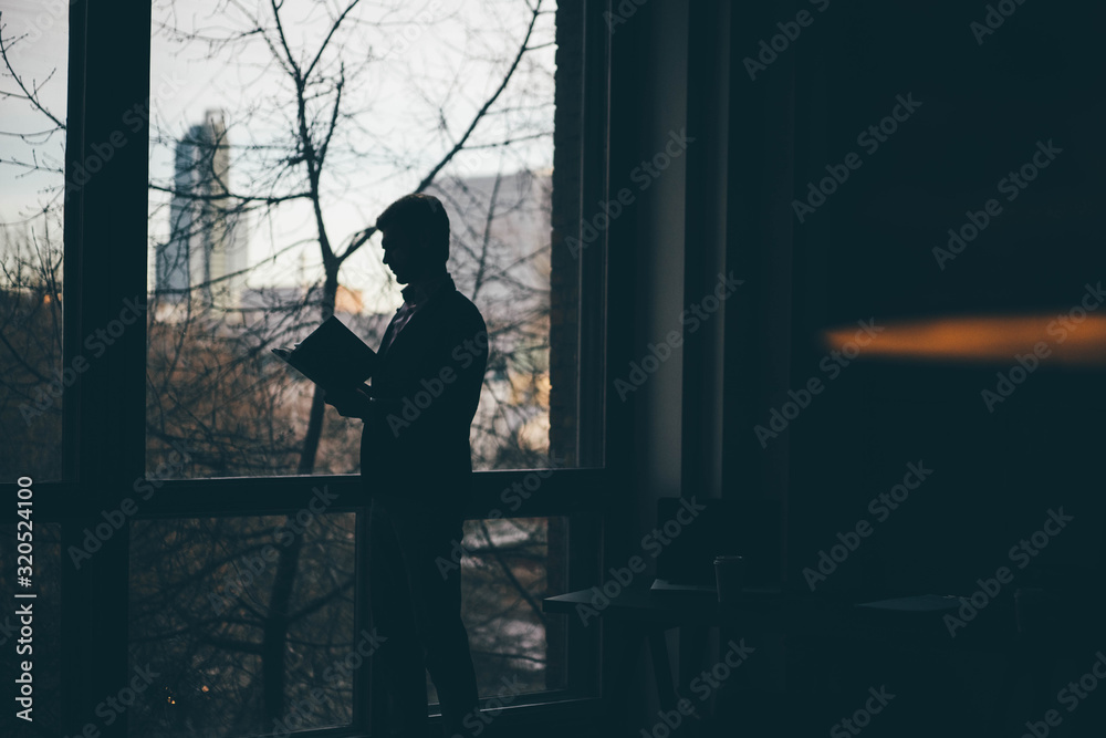 Businessman with paper standing near the office window and reading documents.