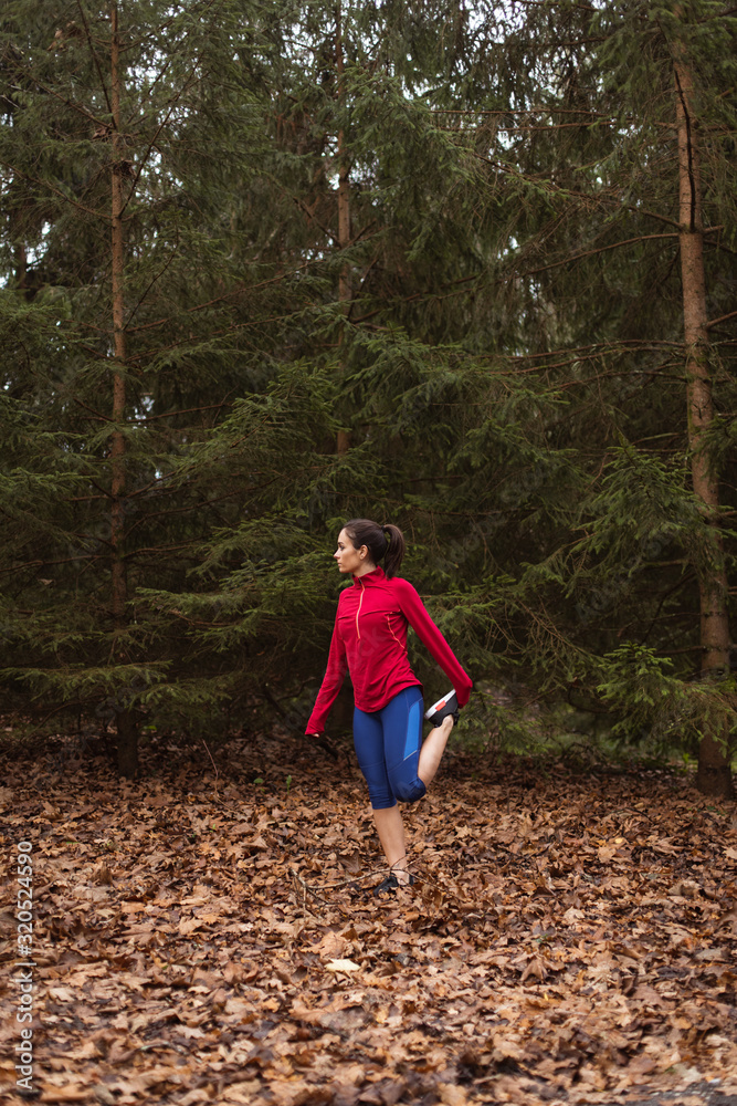 Sporty young woman training in autumn season at the park. Female runner exercising and stretching quadriceps outdoor. Sporty young woman training in autumn season at the park. Female runner exercising and stretching quadriceps outdoor.