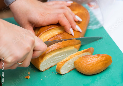 hands of a girl with a beautiful manicure cut a knife with white bread