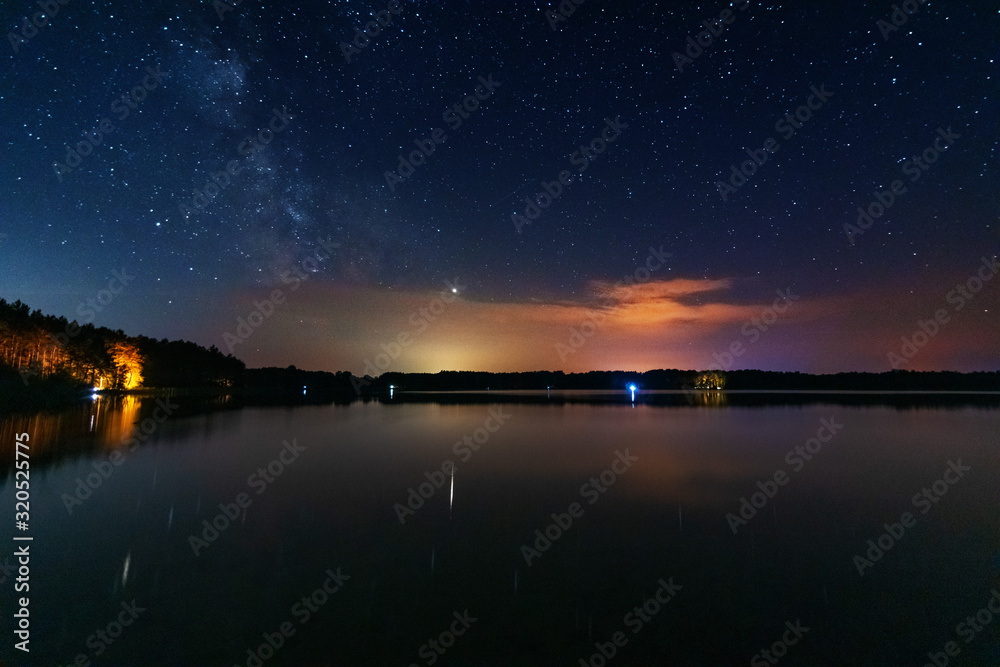 A magical starry night on the river bank with a large tree and a milky way in the sky and falling stars in the summer.	